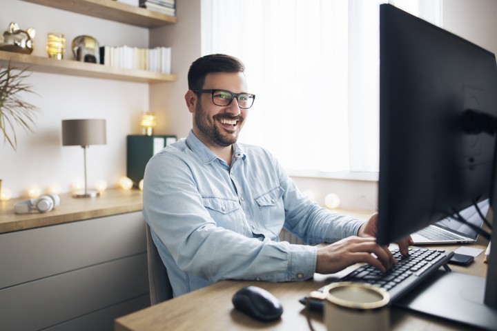 ein Mann lächelt vor dem Bildschirm in seinem Homeoffice
